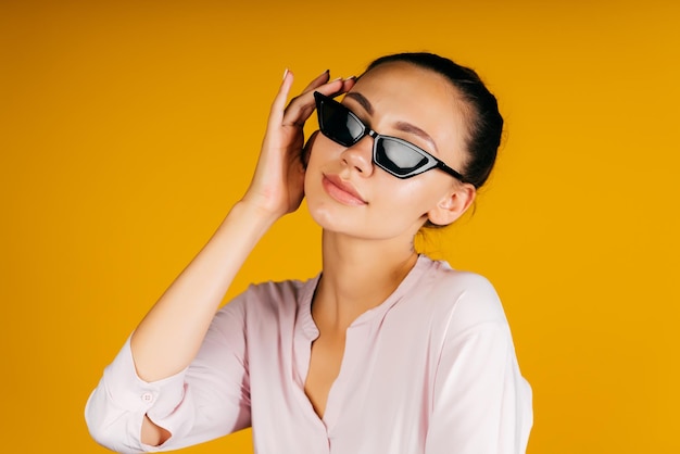 A student in black glasses gracefully raised her hand to the temple of glasses on a yellow background