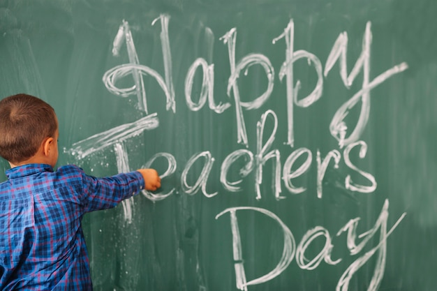 Student boy writing happy teachers day on blackboard