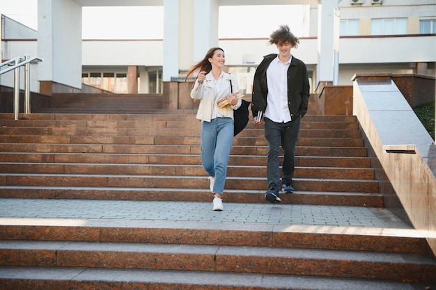 Student couple talking outdoors holding books notes and other learning materials