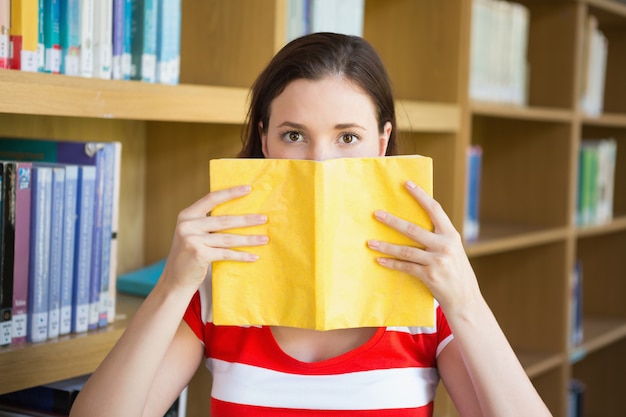 Student covering face with book in library