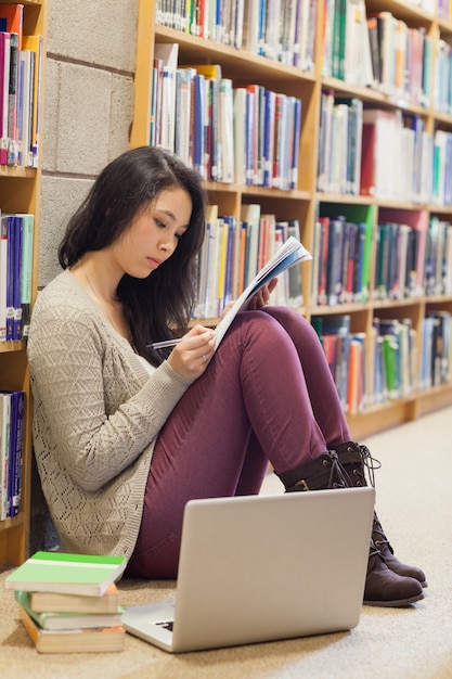 Student die bij de muurzitting op bibliotheekvloer leunt