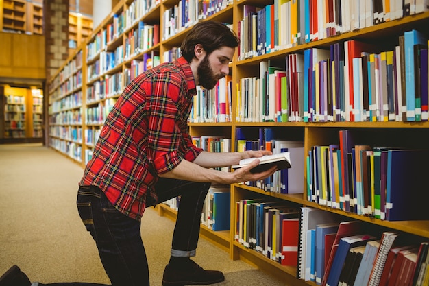 Student die een boek van plank in bibliotheek plukt