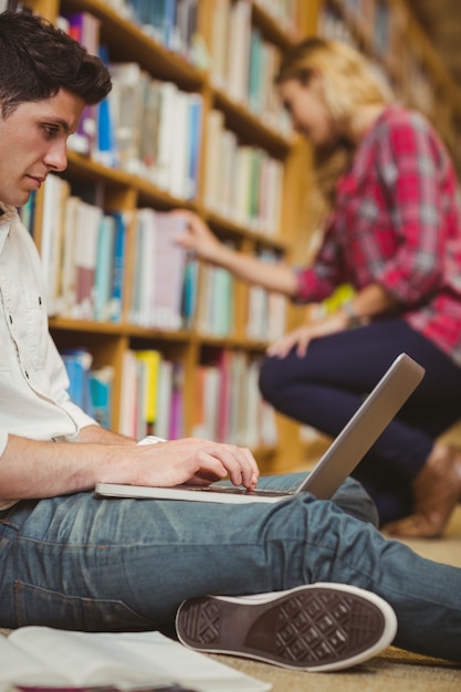 Student die laptop op vloer in bibliotheek met behulp van