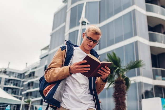 Student die met het boek van de rugzaklezing door modern hotel op tropisch strand lopen