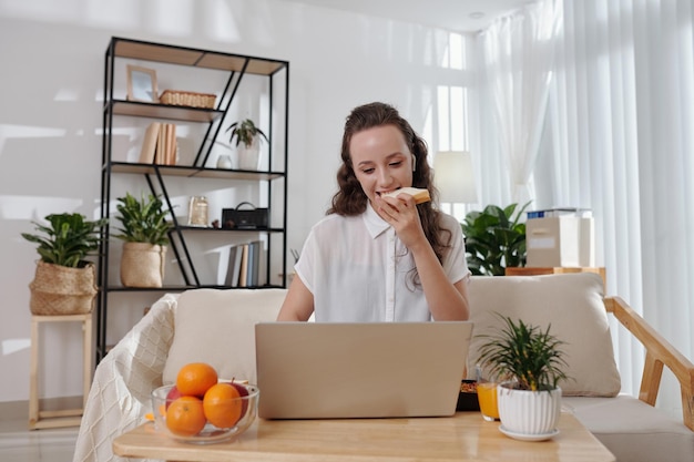 Student die sandwich eet en online lezing op laptop kijkt