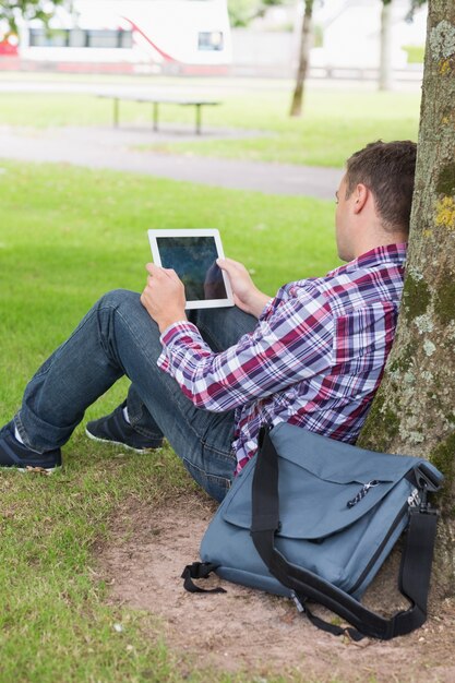 Student die zijn tabletpc buiten gebruiken die op boom leunen