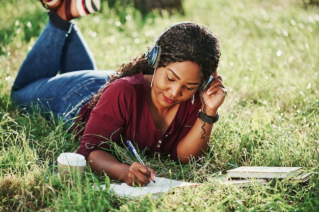 Student doet huiswerk buiten vrolijke Afro-Amerikaanse vrouw in het park in de zomer