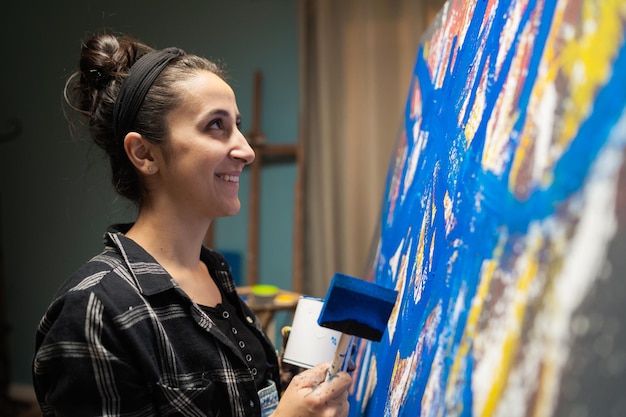 A student dressed in a plaid shirt smiles during an art class as she paints an abstract modern paint