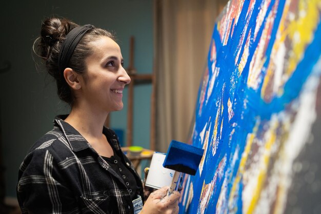 Photo a student dressed in a plaid shirt smiles during an art class as she paints an abstract modern paint