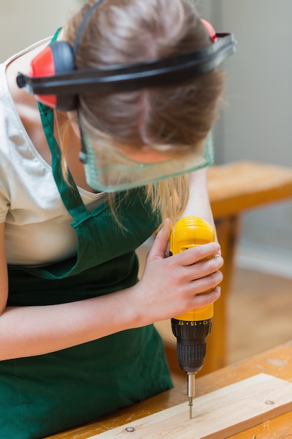 Student drilling a hole in a wooden board at the workbench