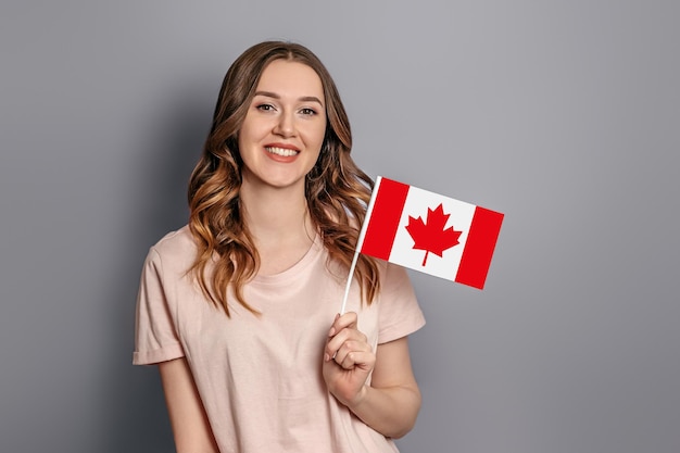 Student exchange Caucasian young student girl holds a small canada flag isolated over orange background Canada day holiday confederation anniversary copy space