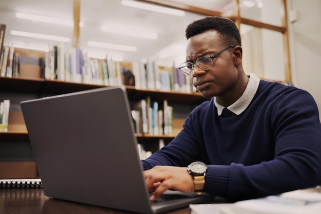 Студент расстроен и чернокожий мужчина набирает на ноутбуке в университете или колледже в гневе из-за проекта онлайн-учения и молодой человек готовится к экзамену в Интернете или делает исследования