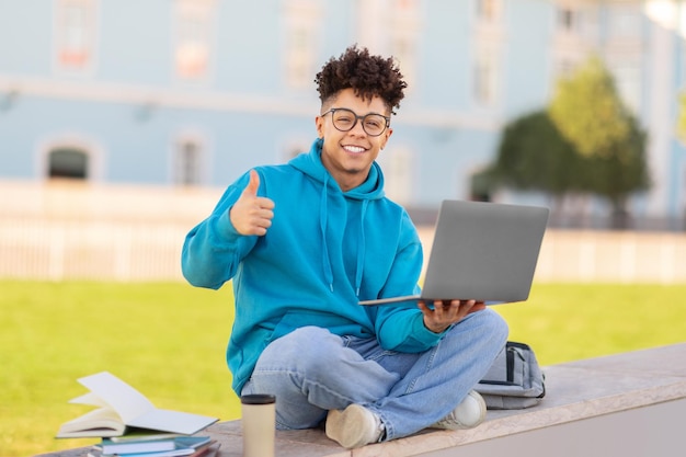 Student geeft duimen omhoog met laptop studeert in het park