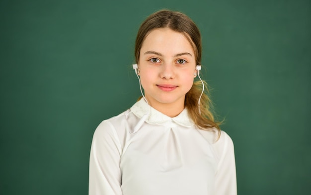 Student girl in headphones at chalkboard background copy space Homeschooling online education Audio translation Audio learning concept Girl in earphones listening to music Listening audio book