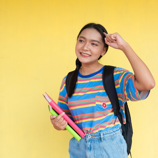 Student girl hold book and smiling on yellow background