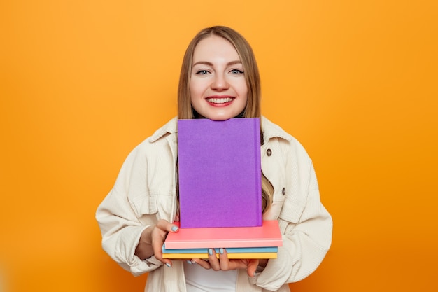 student girl holding a lot of books in her hands isolated on orange studio background