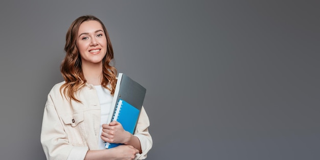 Student girl holding a notebook notepad a folder in her hands smiling and looking at the camera on a dark grey background