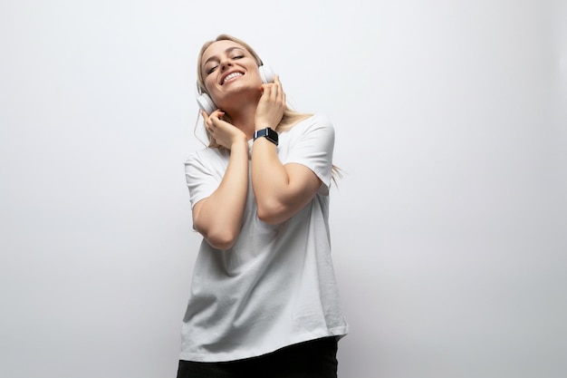 Student girl listening to music with wireless headphones in a studio with white walls