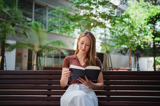 Student girl reading while she takes a break from classes She is sitting on a bench at the campus