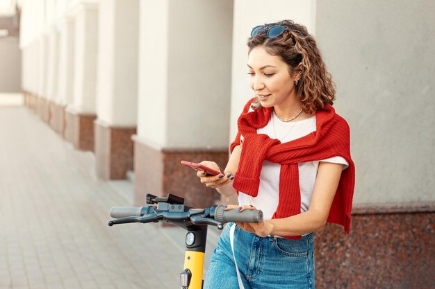 A student girl rents an electric scooter and unlocks it using an app on her smartphone Sharing economy and modern urban transport