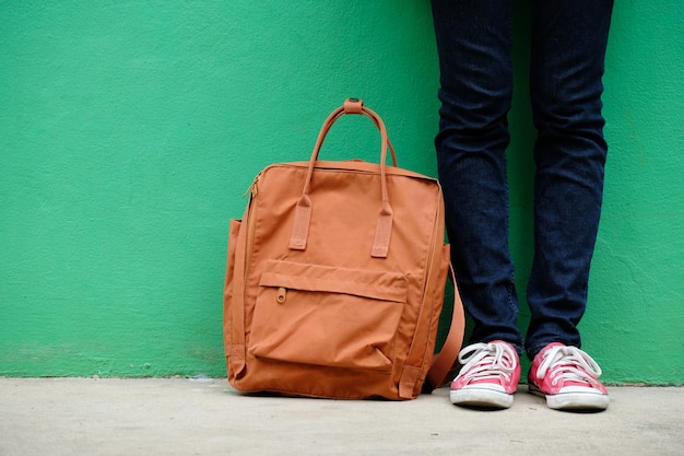 Student girl and school bag standing over green wall background with copy space