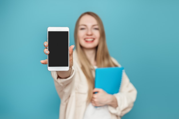 student girl shows a blank screen of a mobile phone at the camera and smiles