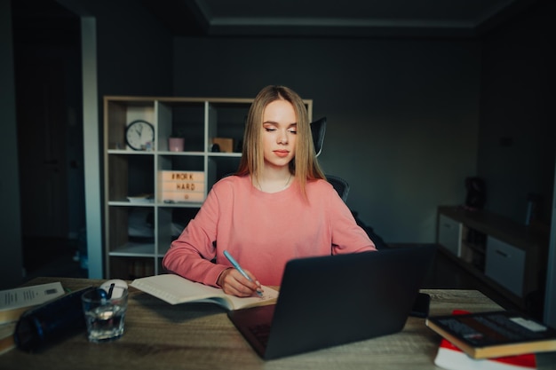 Studentessa seduta a casa a una scrivania con un laptop e studia online guardando lo schermo