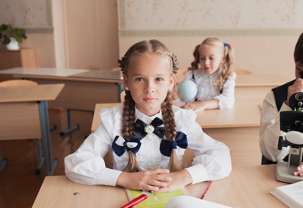 机に座って先生の話を聞いているテーブルに座っている学生の女の子。