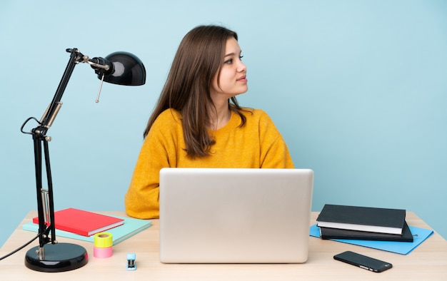 Student girl studying in her house on blue wall in lateral position