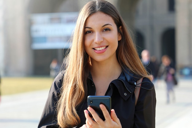 Student girl typing on smart phone out of school looking at camera