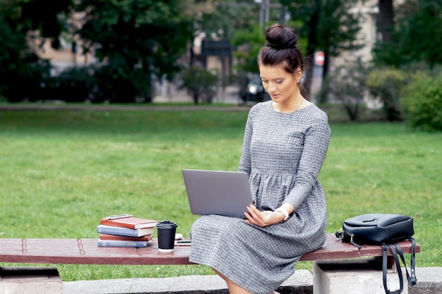 Ragazza dello studente che utilizza computer portatile sul banco nel parco.