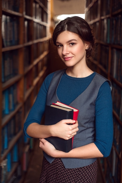 Student girl with books between bookshelves