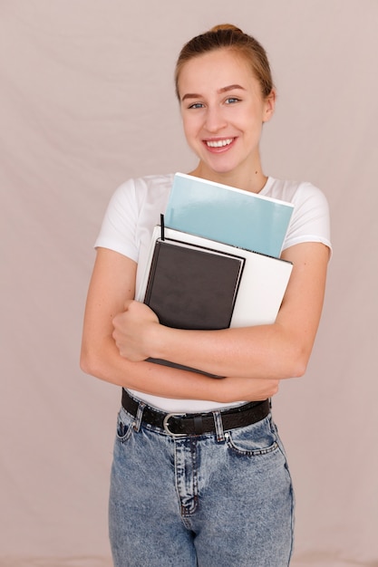 Foto ragazza dell'allievo con i libri in mano sul beige