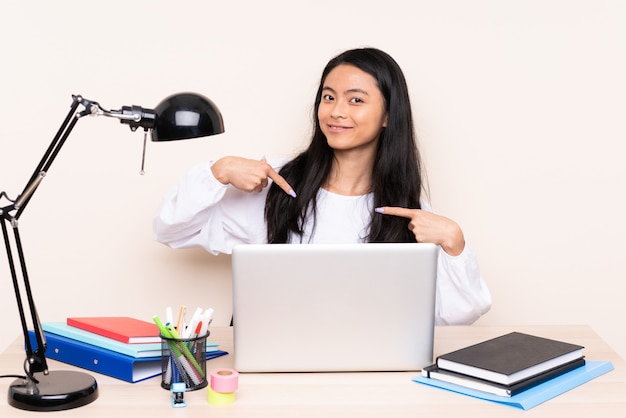 Ragazza dello studente in un posto di lavoro con un computer portatile isolato su fiero beige e soddisfatto di sé