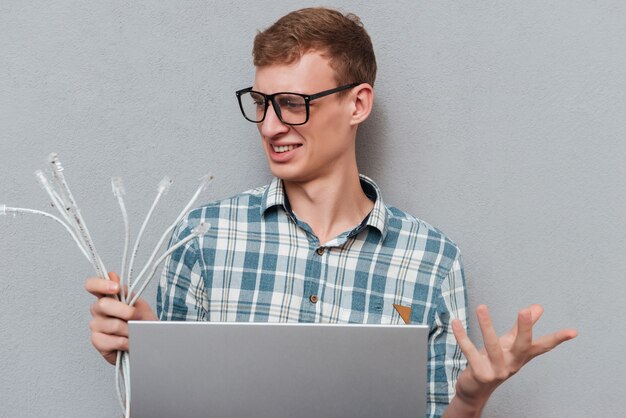 Foto studente in bicchieri con laptop con cavi isolati su grigio