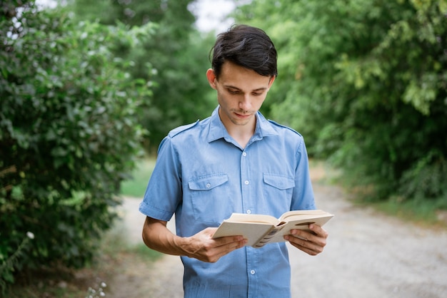 Student guy in a blue shirt with a book in his hand in the park reads