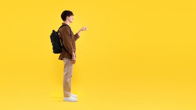 黄色の背景の空スペースで指を指している学生の男