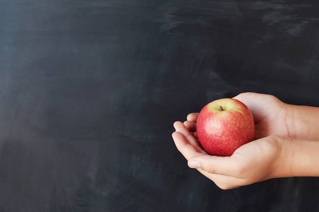 Student hands holding red apple with blackboard background