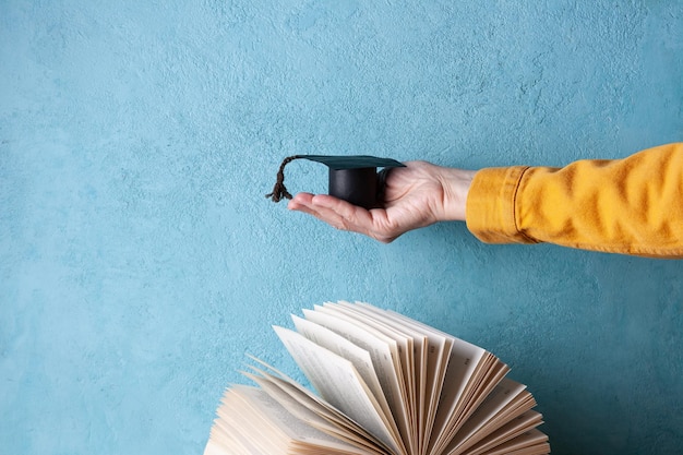 Student hat made of paper in a woman\'s palm over an open book\
space for text