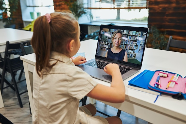 Photo student having video class remotely with her teacher on laptop sitting at desk in classroom