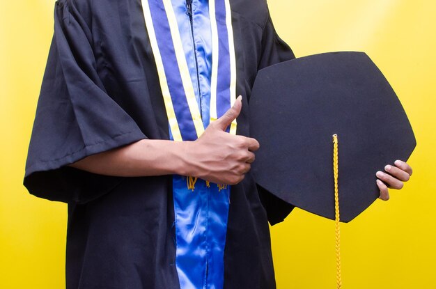 a student holding graduation cap isolated over yellow background