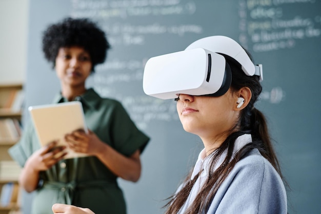 Student in vr-bril die tijdens de les zit met leraar die materiaal op de achtergrond uitlegt