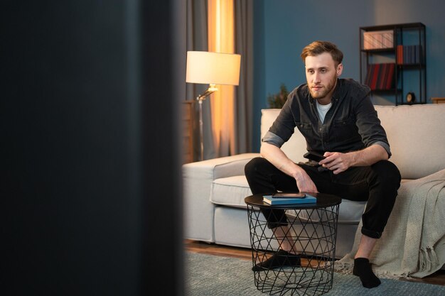 A student is resting on a sofa in a living room next to him
there is a coffee table with a book