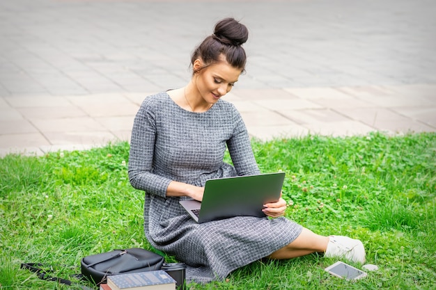 Student jonge blanke vrouw gebruikt laptop zittend op het gras op straat