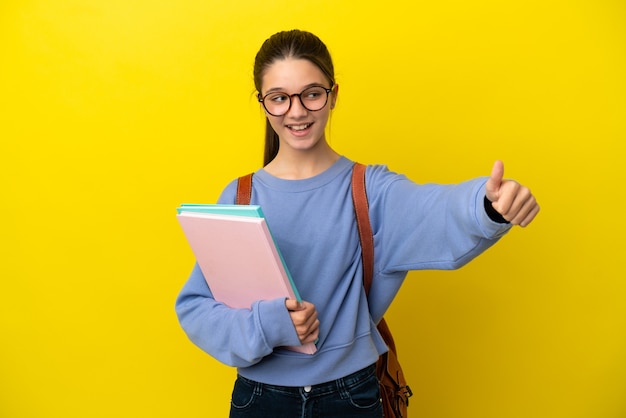 親指を立てるジェスチャーを与える孤立した黄色の背景上の学生の子供の女性