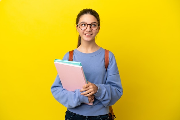 見上げながらアイデアを考えている孤立した黄色の背景上の学生の子供の女性