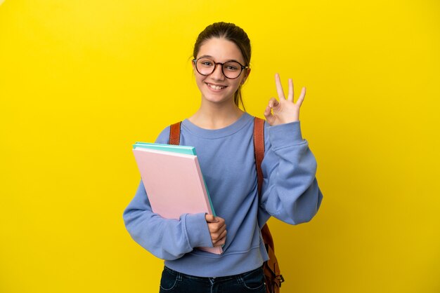 Student kind vrouw over geïsoleerde gele achtergrond met ok teken met vingers