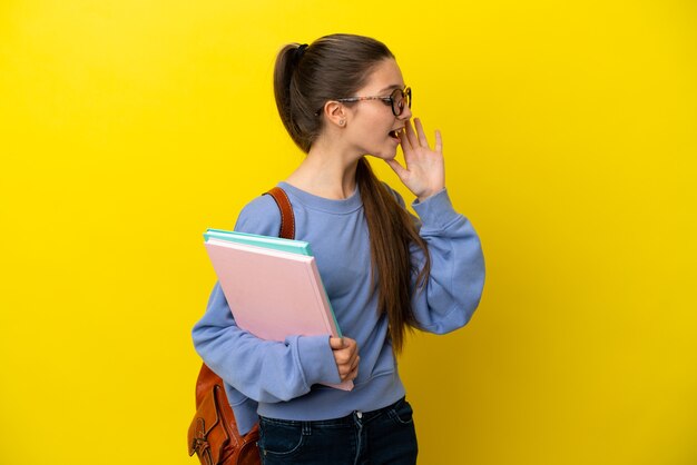 Student kind vrouw over geïsoleerde gele muur schreeuwen met mond wijd open naar de zijkant