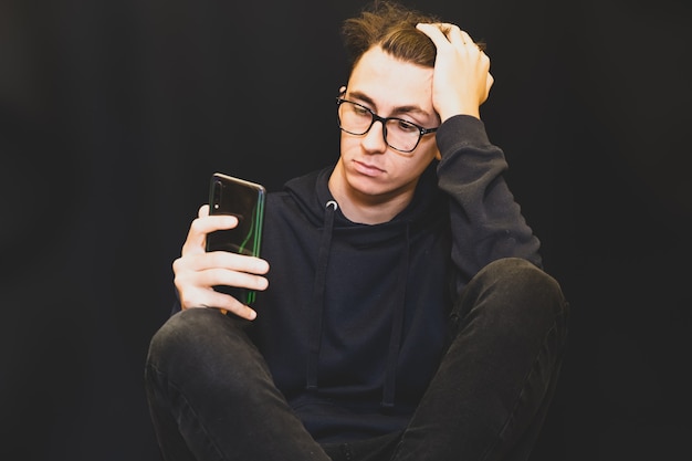 Student lijden met smartphone, donkere kleren op donkere achtergrond. Geestelijke gezondheid lijden.