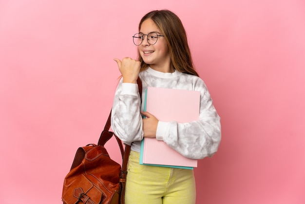 Studentessa bambina su sfondo rosa isolato che punta al lato per presentare un prodotto